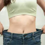 Mulher mostrando a calça folgada na cintura como resultado do emagrecimento.