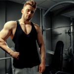 Pessoa fazendo pose na academia, exibindo corpo definido e musculatura evidente, em ambiente de treino com aparelhos ao fundo, transmitindo disciplina, consistência e foco em hipertrofia e definição muscular.